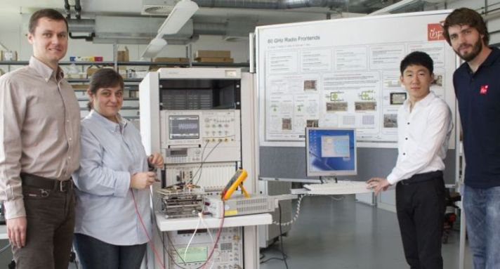 Standing in front of a large poster of 60GHz radio fundamentals this design and development team is creating ISM applications for highspeed data and video streaming at millimeterwave frequencies Photo courtesy of IHP Microelectronics