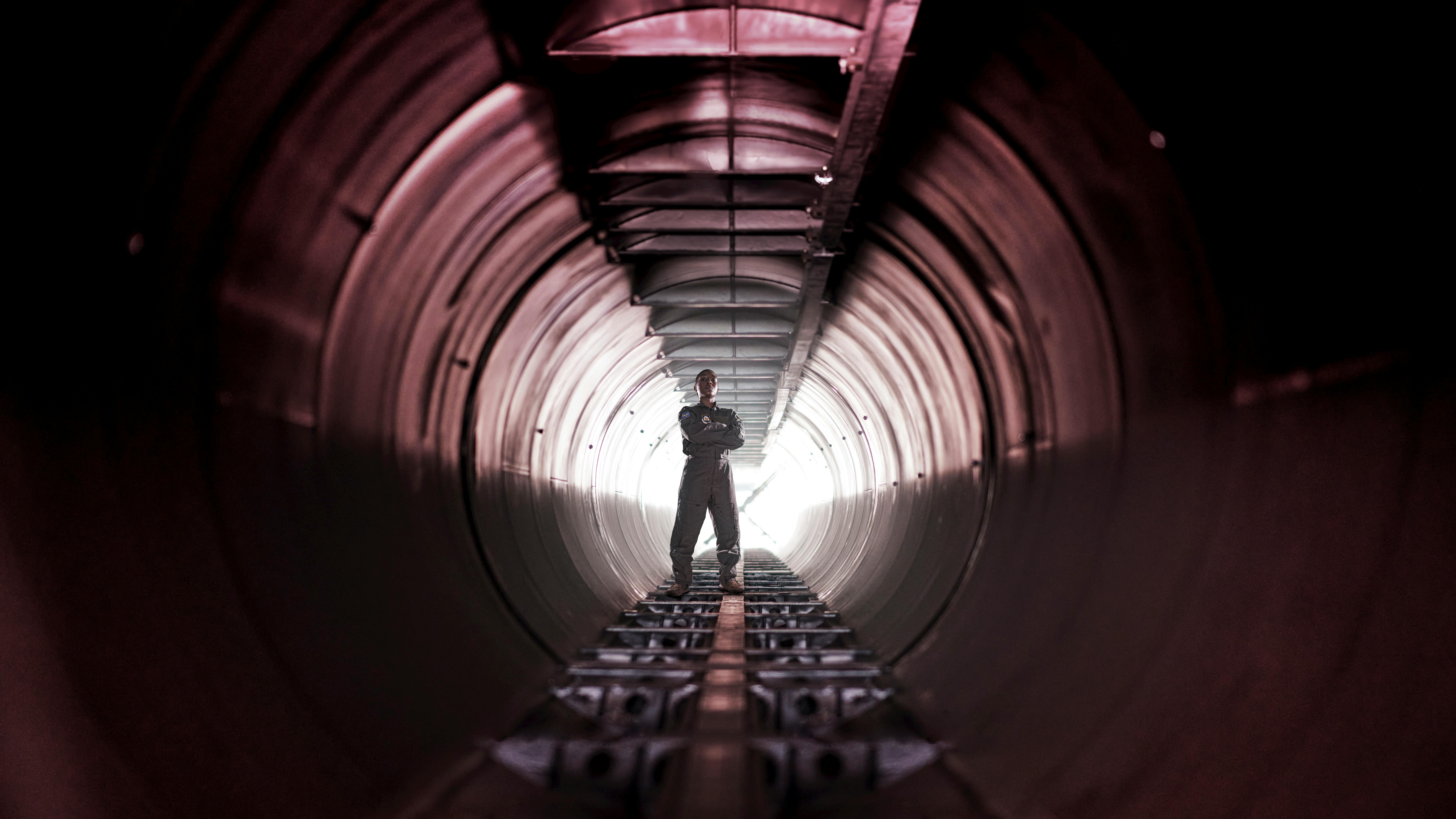 Man stands, arms folded, within a large tunnel.