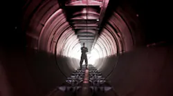 Man stands, arms folded, within a large tunnel.